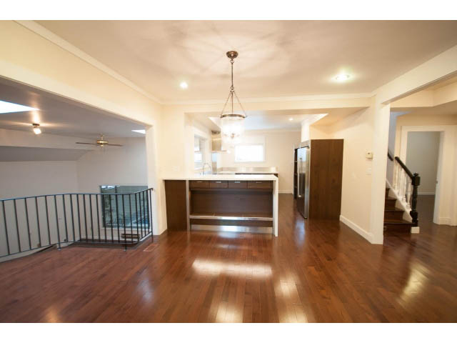 Spacious living room with hardwood floors and a chandelier, leading to a kitchen with white countertops. - Main - 4149 Osler St, Vancouver West Side