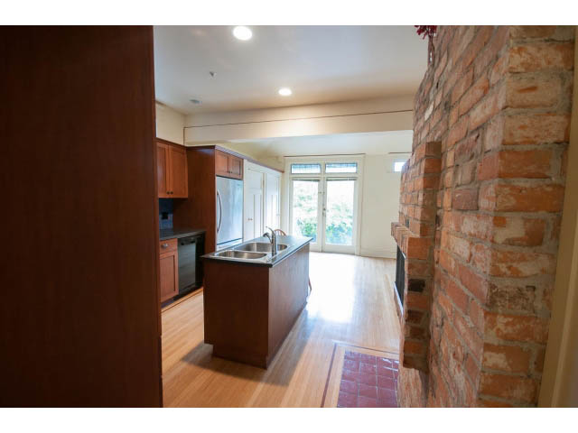 Bright kitchen with wooden cabinets, hardwood floors, and a brick wall. - 3362 West 3rd Ave, Vancouver West Side