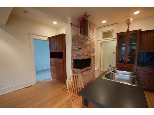 Bright kitchen with dark countertops, hardwood floors, and a brick fireplace. - 3362 West 3rd Ave, Vancouver West Side