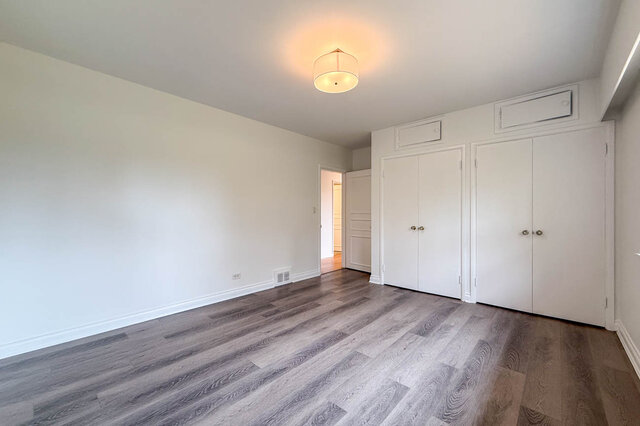 Empty bedroom with grey wood-look flooring and white built-in closet doors under a warm pendant light. - 555 Stevens Drive, West Vancouver
