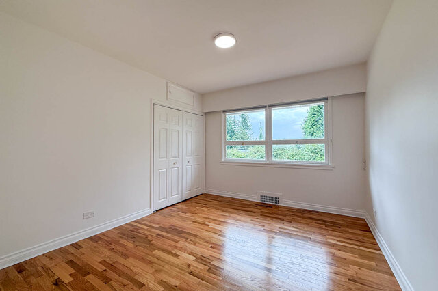 Empty bedroom with glossy parquet hardwood floors and a window framing lush green tree views. - 555 Stevens Drive, West Vancouver