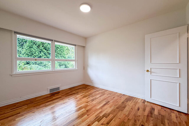 Empty room with warm hardwood parquet floors and a window framing a lush green tree view. - 555 Stevens Drive, West Vancouver