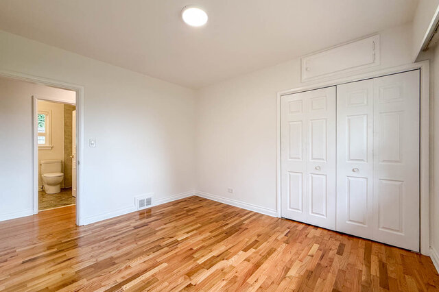 Empty bedroom with parquet hardwood floors and white double closet doors, with a doorway to an adjacent bathroom. - 555 Stevens Drive, West Vancouver