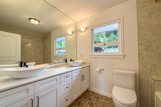 Bright bathroom with white vanity, marble countertops, dual vessel sinks, and a window overlooking greenery. - 555 Stevens Drive, West Vancouver