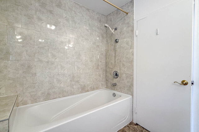 Bathroom with a white soaking tub set against beige marble-look tile walls and chrome shower fixtures. - 555 Stevens Drive, West Vancouver