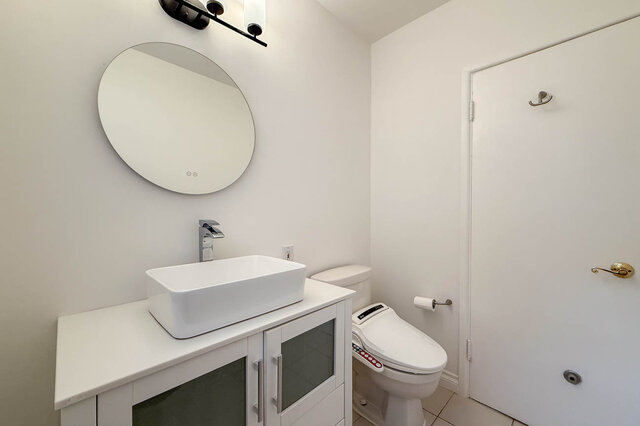 Bathroom with a round frameless mirror, white vessel sink, and frosted-glass vanity cabinets. - 555 Stevens Drive, West Vancouver