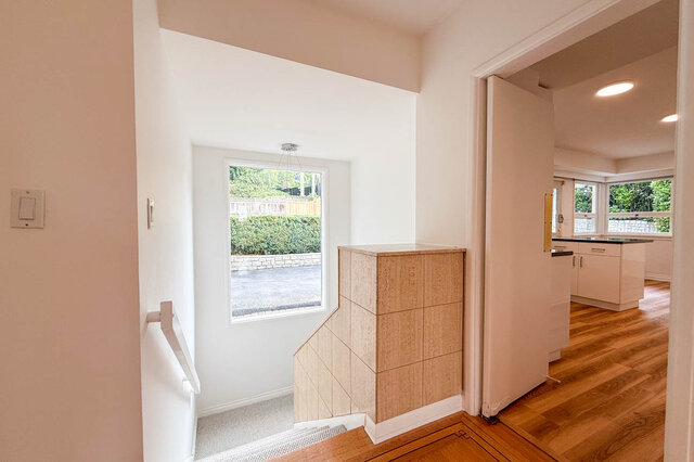 Stair landing with built-in wood cabinetry, hardwood floors, and a window overlooking greenery. - 555 Stevens Drive, West Vancouver