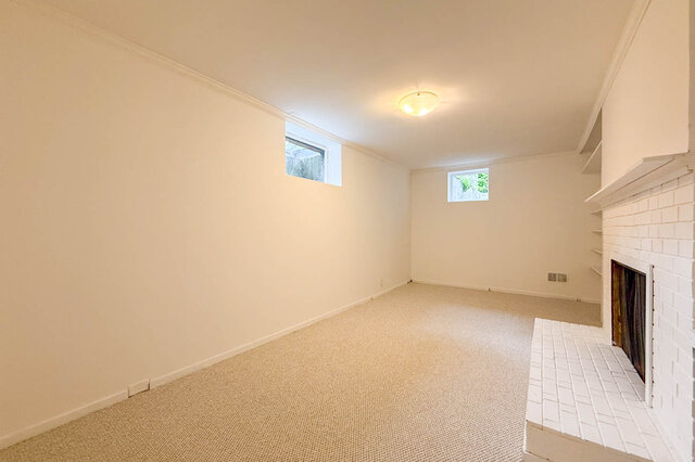 Spacious carpeted living room featuring a white brick fireplace with built-in shelving and high windows. - 555 Stevens Drive, West Vancouver