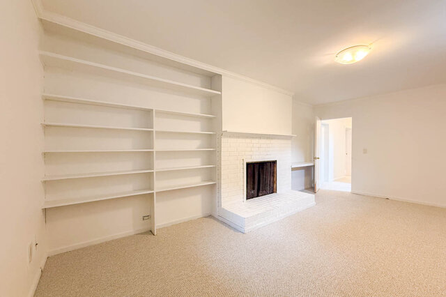 Spacious living room with white built-in shelving and a white brick fireplace on carpeted floors. - 555 Stevens Drive, West Vancouver