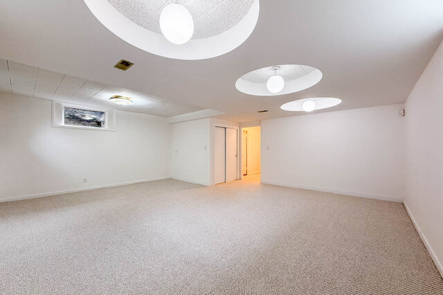 Spacious carpeted room with circular recessed ceiling lights and a doorway leading to a warmly lit hallway. - 555 Stevens Drive, West Vancouver