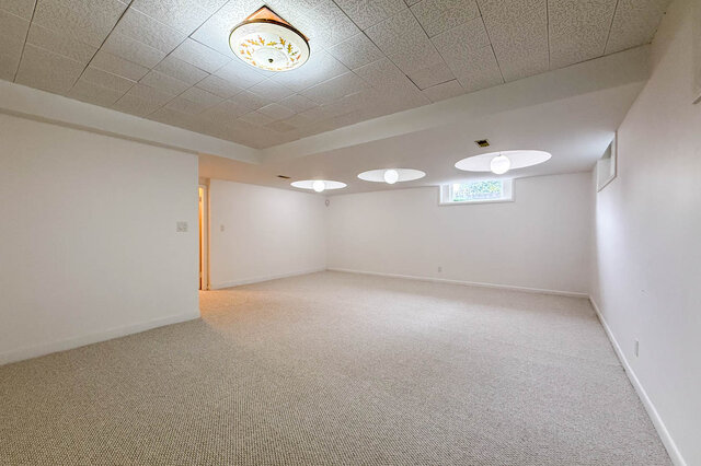 Spacious carpeted room with a drop ceiling, decorative light fixture, and recessed globe lighting. - 555 Stevens Drive, West Vancouver