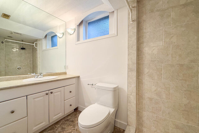 Clean bathroom with white vanity, beige tile walls, and a frosted arched window. - 555 Stevens Drive, West Vancouver