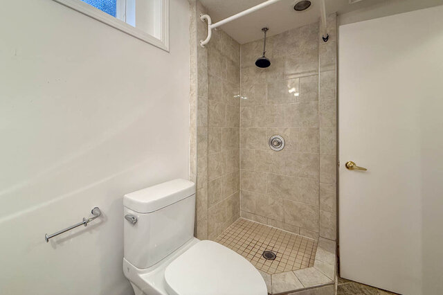 Bathroom featuring a walk-in shower with beige tile walls and a mosaic tile floor, plus a white toilet and grab bar.