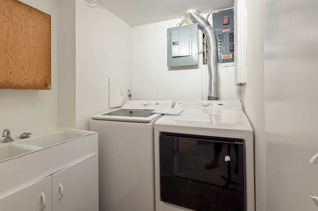 Laundry room with white washer and dryer, a utility sink, and an exposed electrical panel. - 555 Stevens Drive, West Vancouver