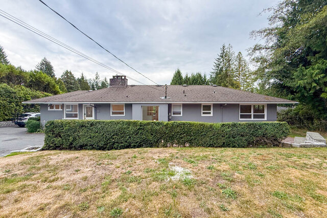 Exterior of a single-story home with gray siding, a brick chimney, and a tall trimmed hedge along the front yard. - 555 Stevens Drive, West Vancouver