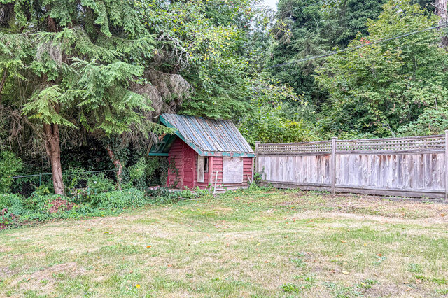 Backyard with a small red shed, weathered wooden fence, and overgrown lawn bordered by mature trees. - 555 Stevens Drive, West Vancouver