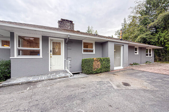 Gray single-story house exterior with white stained-glass front door, brick chimney, and paved driveway. - 555 Stevens Drive, West Vancouver