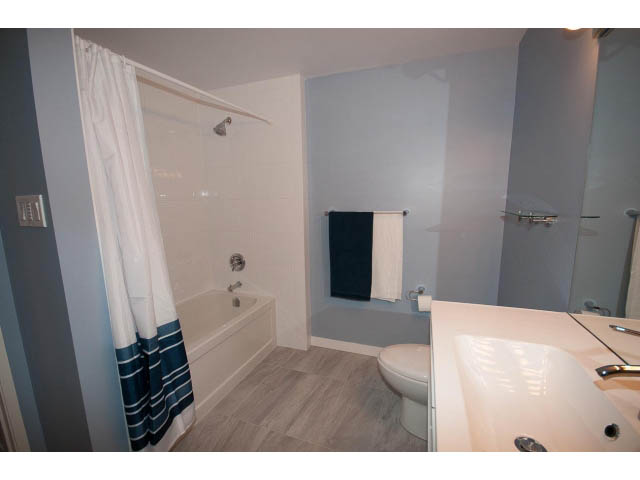 Bright bathroom with white fixtures, hardwood floors, and a shower curtain. - 14 - 1201 Lamey's Mill Rd., Vancouver West Side