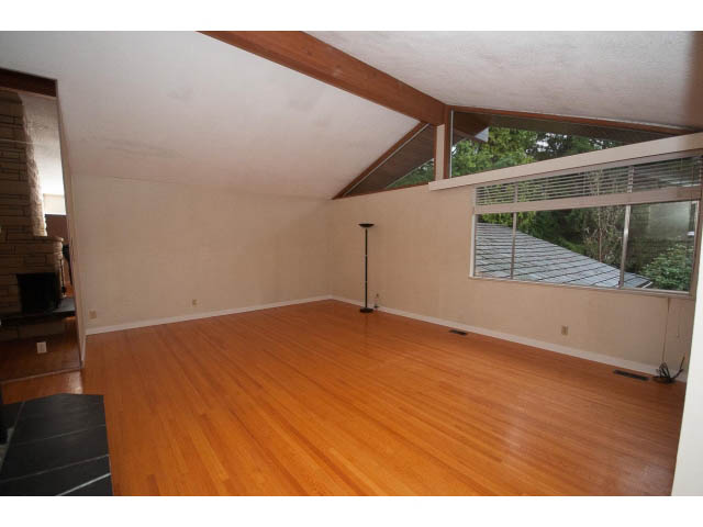 Bright living room with hardwood floors and large windows, offering a view of the roof and trees. - 610 Newdale Rd., West Vancouver