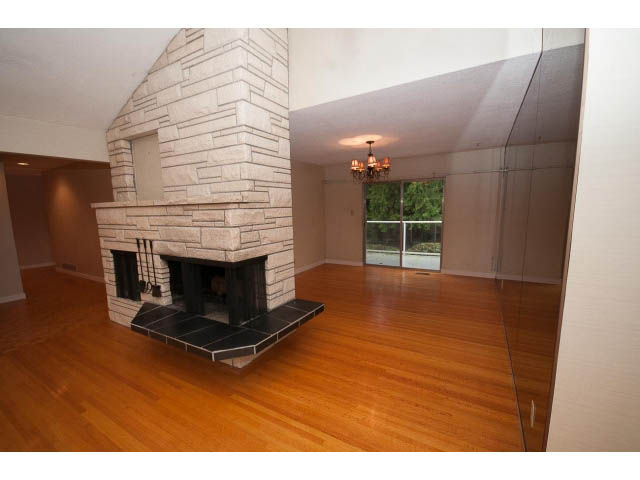 Living room with stone fireplace, hardwood floors, and a large window. - 610 Newdale Rd., West Vancouver