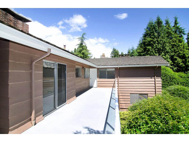 Bright patio with sliding glass door and greenery, leading to a wooden deck. - 610 Newdale Rd., West Vancouver