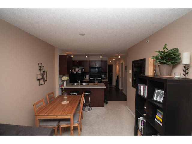 Open-concept living space with wooden dining table, dark cabinetry, and a cozy corner with a bookshelf and potted plant.