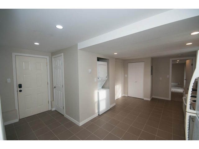 Bright kitchen with tiled floors and white cabinetry, leading to a living area. - Suite - 1719 Peters Rd, North Vancouver