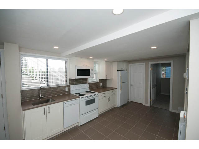 Bright kitchen with white appliances and tiled floors, featuring a large window and a view of the outdoors. - Suite - 1719 Peters Rd, North Vancouver