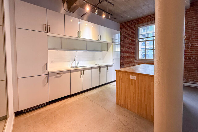 Modern kitchen with white cabinets, concrete countertops, and exposed brick wall. - 308 - 546 Beatty Street, Vancouver Downtown