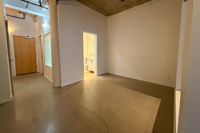 Spacious loft with polished concrete floors and exposed beams, leading to a bathroom. - 308 - 546 Beatty Street, Vancouver Downtown