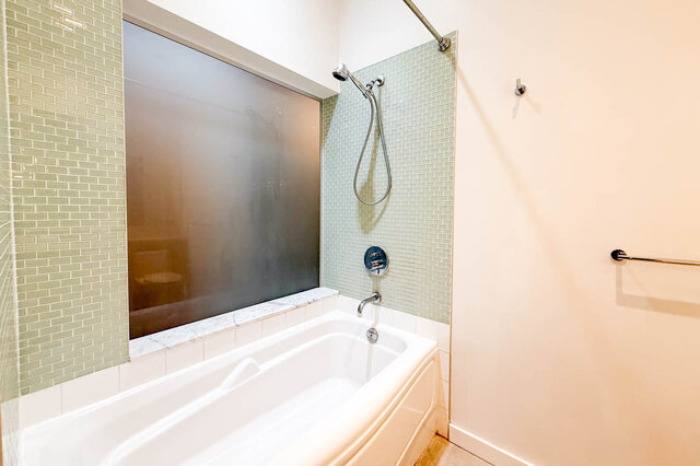 Spacious bathroom with a modern tub and shower combo, featuring sleek tile accents and a sleek showerhead.