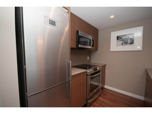 Bright kitchen with stainless steel appliances, hardwood floors, and a modern artwork on the wall. - 1602 - 135 East 17th Street, North Vancouver