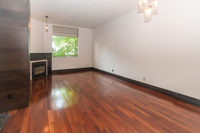 Bright living room with hardwood floors and a fireplace, natural light from a window. - 102 - 1970 Haro St, Vancouver Downtown
