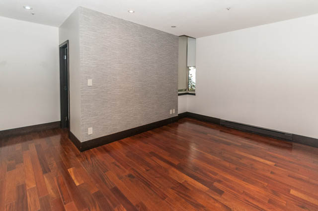 Bright living room with hardwood floors and a textured accent wall. - 102 - 1970 Haro St, Vancouver Downtown