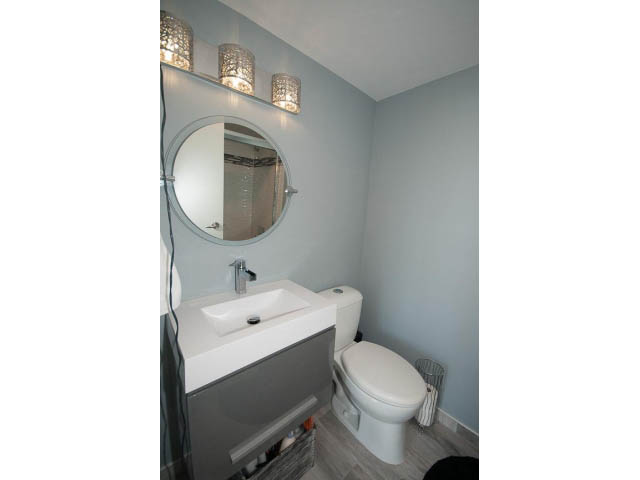 Bright bathroom with modern sink, toilet, and vanity, light blue walls, and a round mirror. - 1502 - 907 Beach Ave, Vancouver Downtown