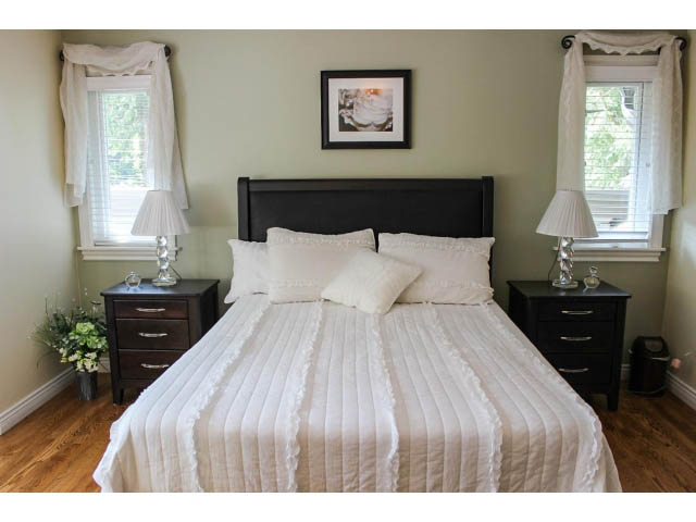 Spacious bedroom with white bedding, black headboard, and wooden floors. - Main - 980 Montroyal Blvd, North Vancouver