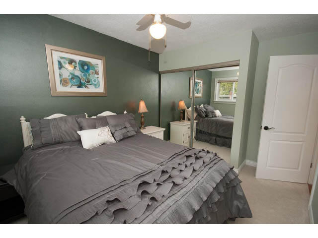 Furnished bedroom with green walls, large mirror, and gray bedding. - Main - 980 Montroyal Blvd, North Vancouver