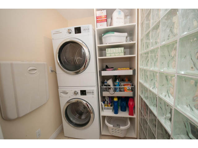 Laundry room with stacked washer and dryer, shelves, and glass block wall. - Main - 980 Montroyal Blvd, North Vancouver