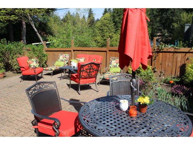 Furnished patio with red furniture and garden decor, surrounded by trees. - Main - 980 Montroyal Blvd, North Vancouver