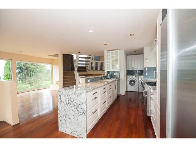 Bright kitchen with granite countertops and hardwood floors, leading to a spacious living area with a city view. - 3890 Sharon Drive, West Vancouver