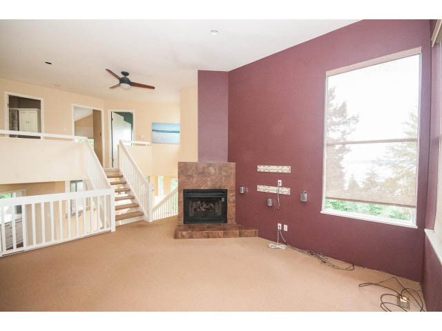 Open living room with exposed brick, large windows, and a fireplace. - 3890 Sharon Drive, West Vancouver