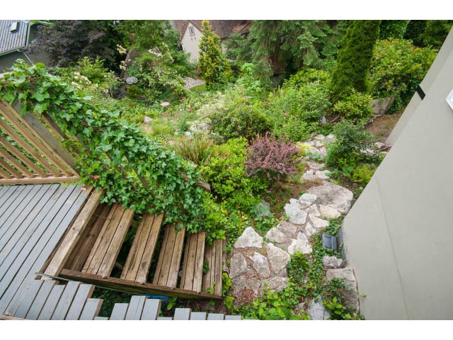 Deck with wooden planks and lush greenery, leading to a stone pathway. - 3890 Sharon Drive, West Vancouver