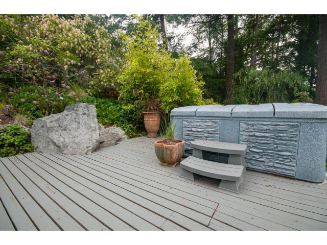 Spacious deck with stone seating and wooden flooring, surrounded by lush greenery. - 3890 Sharon Drive, West Vancouver