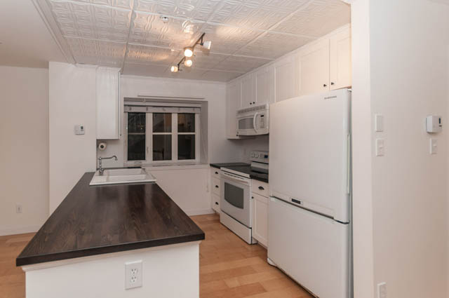 Bright kitchen with dark countertops and hardwood floors, featuring a white refrigerator and microwave. - 2263 Heather st., Vancouver West Side