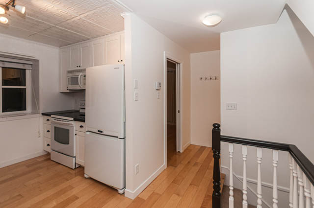 Bright kitchen with white cabinets and hardwood floors, leading to a hallway with a staircase. - 2263 Heather st., Vancouver West Side