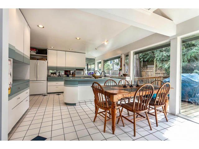 Bright kitchen with white cabinets, tiled floor, and large sliding glass door leading to a deck. - 3243 Milton Ave., North Vancouver