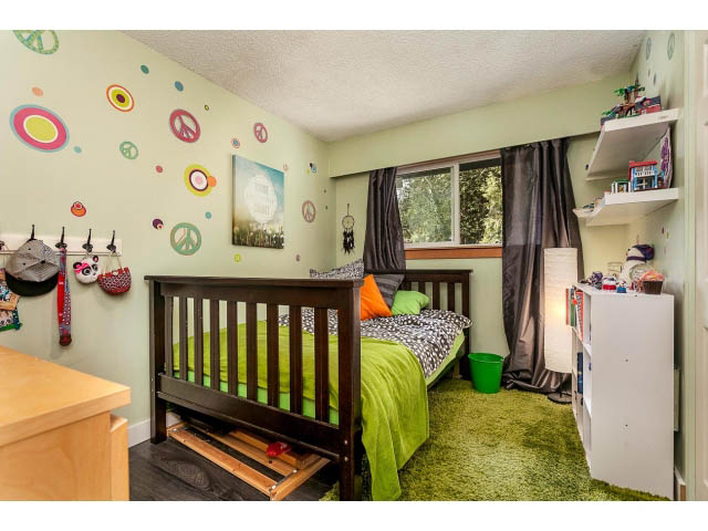Bright bedroom with green carpet, wooden furniture, and colorful wall decorations. - 3243 Milton Ave., North Vancouver