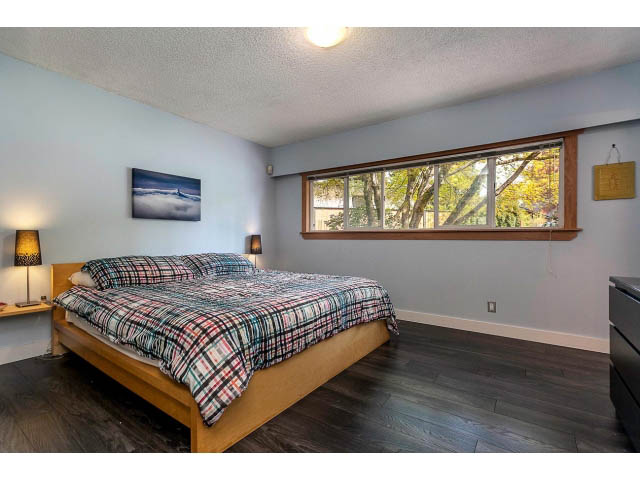 Spacious bedroom with hardwood floors, large windows, and a cozy plaid bedspread. - 3243 Milton Ave., North Vancouver