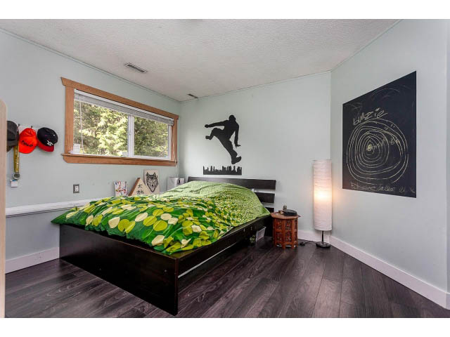 Bright bedroom with hardwood floors, green bedding, and wall art. - 3243 Milton Ave., North Vancouver