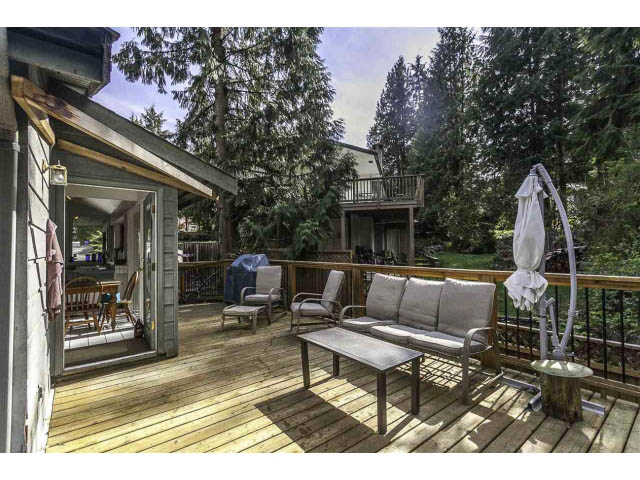 Furnished patio with wooden deck, outdoor furniture, and lush greenery. - 3243 Milton Ave., North Vancouver